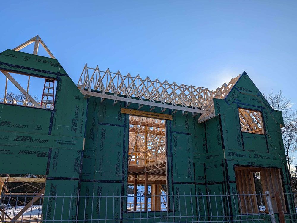 Maison neuve en construction, avec ossature bois, bardage vert et charpente apparente sur fond de ciel bleu azur.