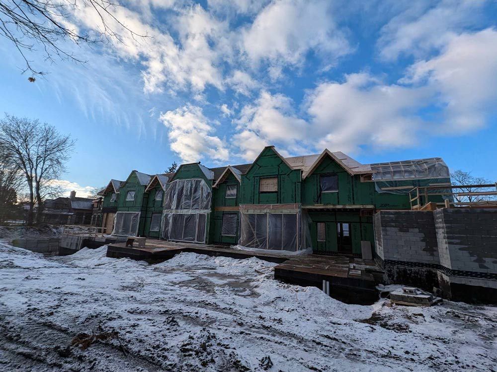Chantier de construction avec des bâtiments à ossature bois sous un ciel nuageux et lumineux, recouvert de neige.