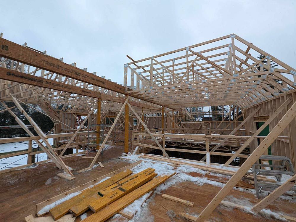 La charpente en bois d'un bâtiment en construction, avec de la neige au sol et un ciel nuageux.
