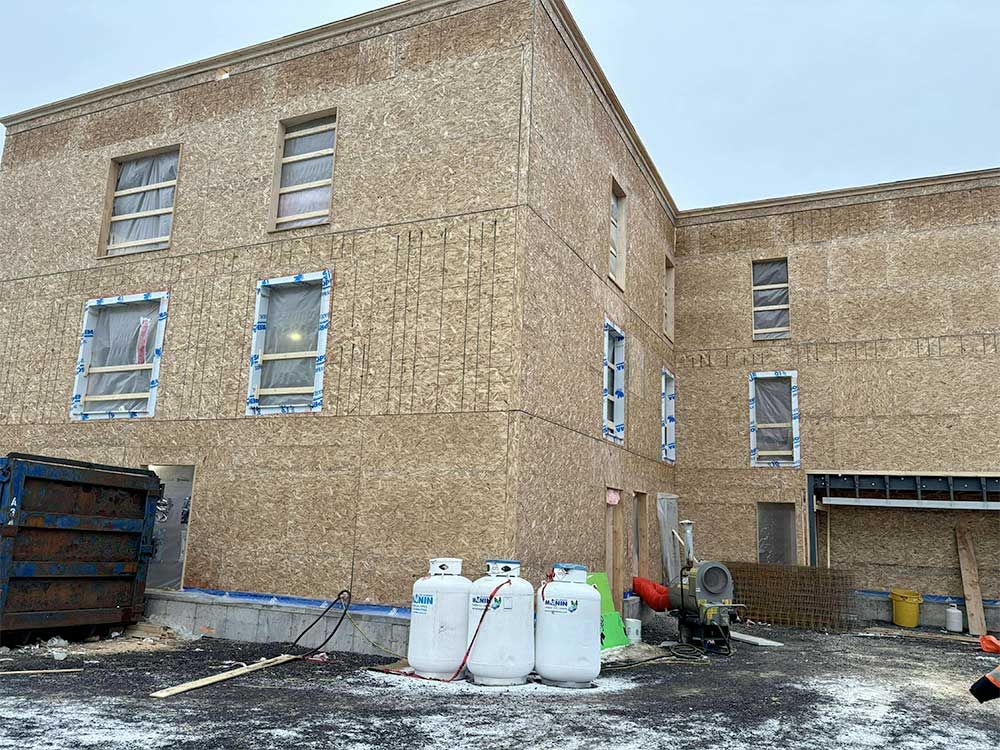 Bâtiment en construction avec bardage en bois, fenêtres recouvertes de ruban adhésif bleu, réservoirs de propane à l'avant.