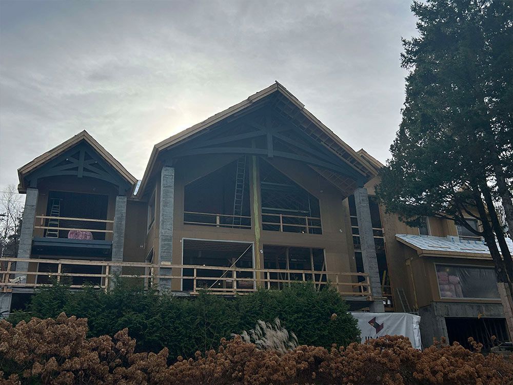 Une grande maison en construction avec des poutres en bois apparentes, des murs inachevés et des échafaudages tout autour.