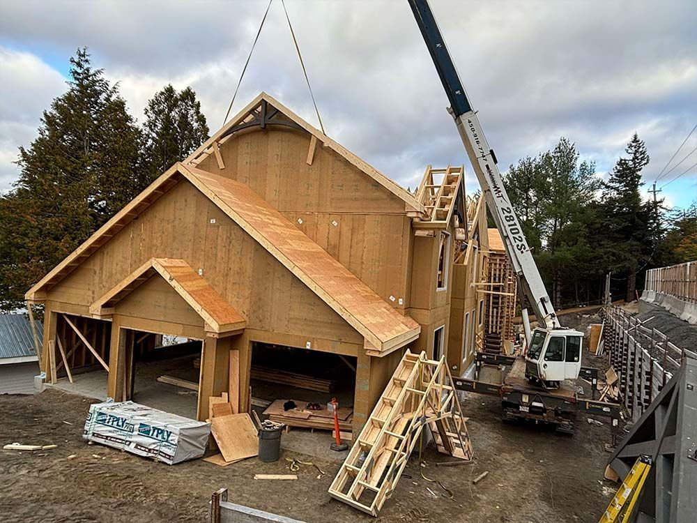 Chantier de construction avec une grue soulevant une section de toiture en bois pour la poser sur un bâtiment.