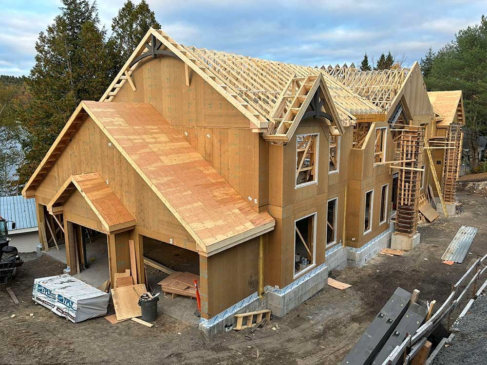 Maison en construction ; charpente en bois, fermes de toit apparentes, échafaudages et matériaux visibles.
