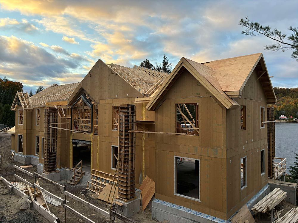 Maison en construction avec charpente en bois apparente et toiture partielle, près de l'eau.