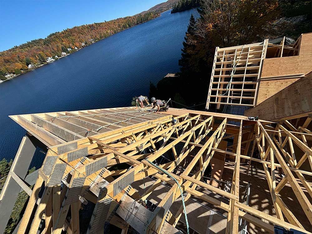Construction de la toiture d'un bâtiment avec des poutres en bois, donnant sur un lac avec des arbres en arrière-plan.
