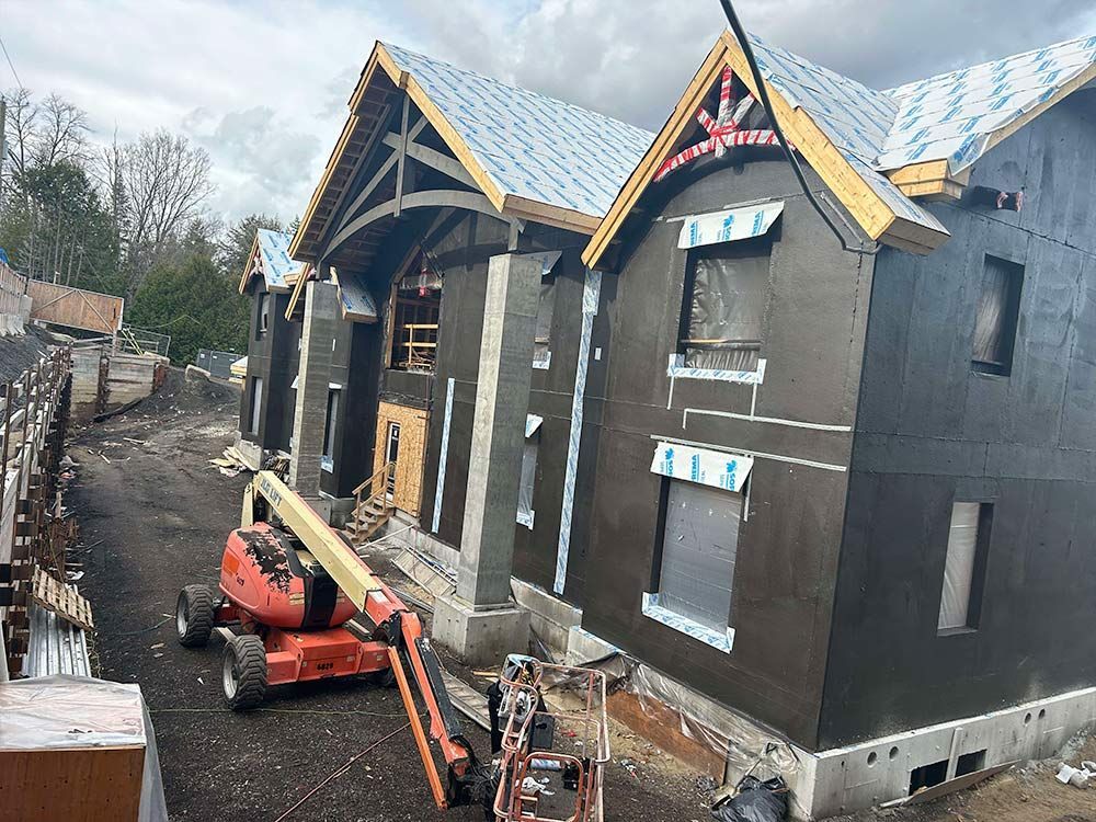 Bâtiment en construction avec bardage foncé, échafaudages et nacelle élévatrice orange ; ciel couvert.