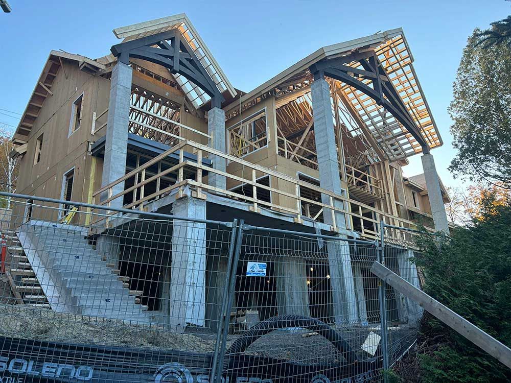 Maison en construction avec charpente apparente en bois et piliers en béton.