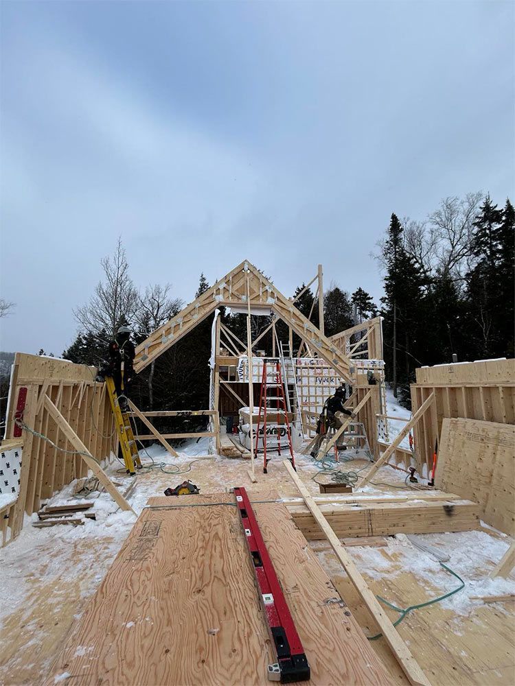 Chantier de construction avec charpente en bois et toiture partiellement construite, en extérieur en hiver.