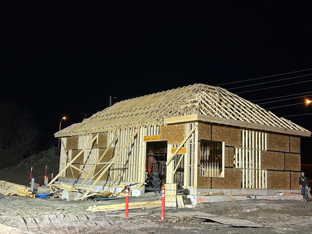 Maison en construction la nuit, avec charpente apparente et environnement sombre.