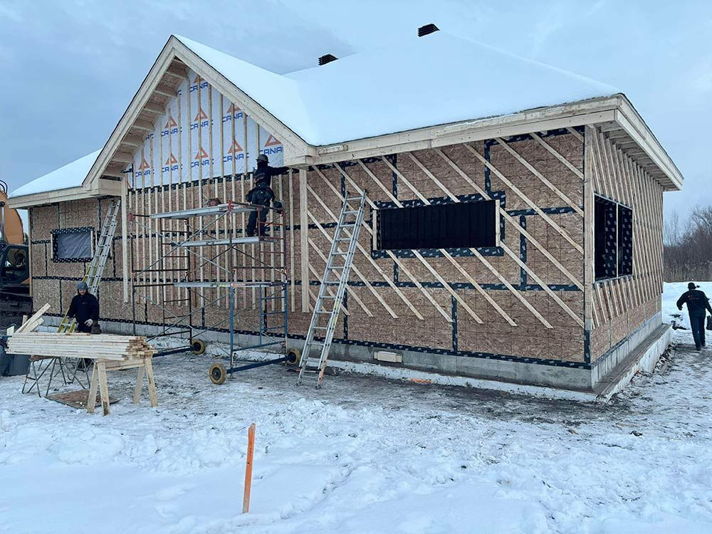 Construction d'une maison en hiver : des ouvriers montent les murs sur un chantier enneigé.