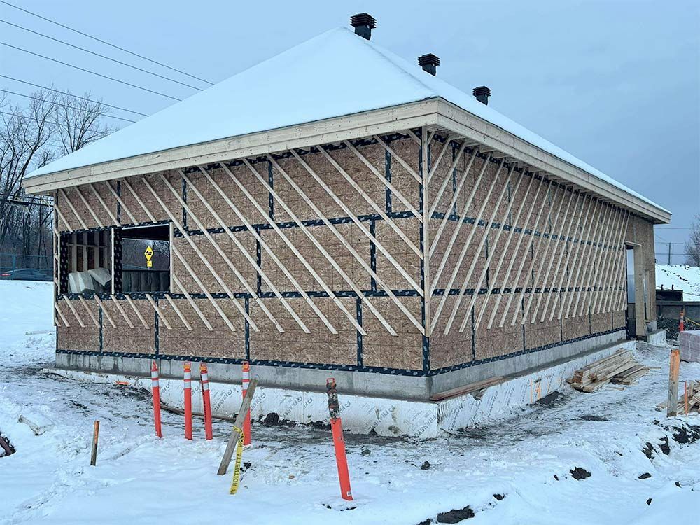 Bâtiment en construction, vue extérieure, avec des contreventements en bois diagonaux sur les murs ; sol enneigé.
