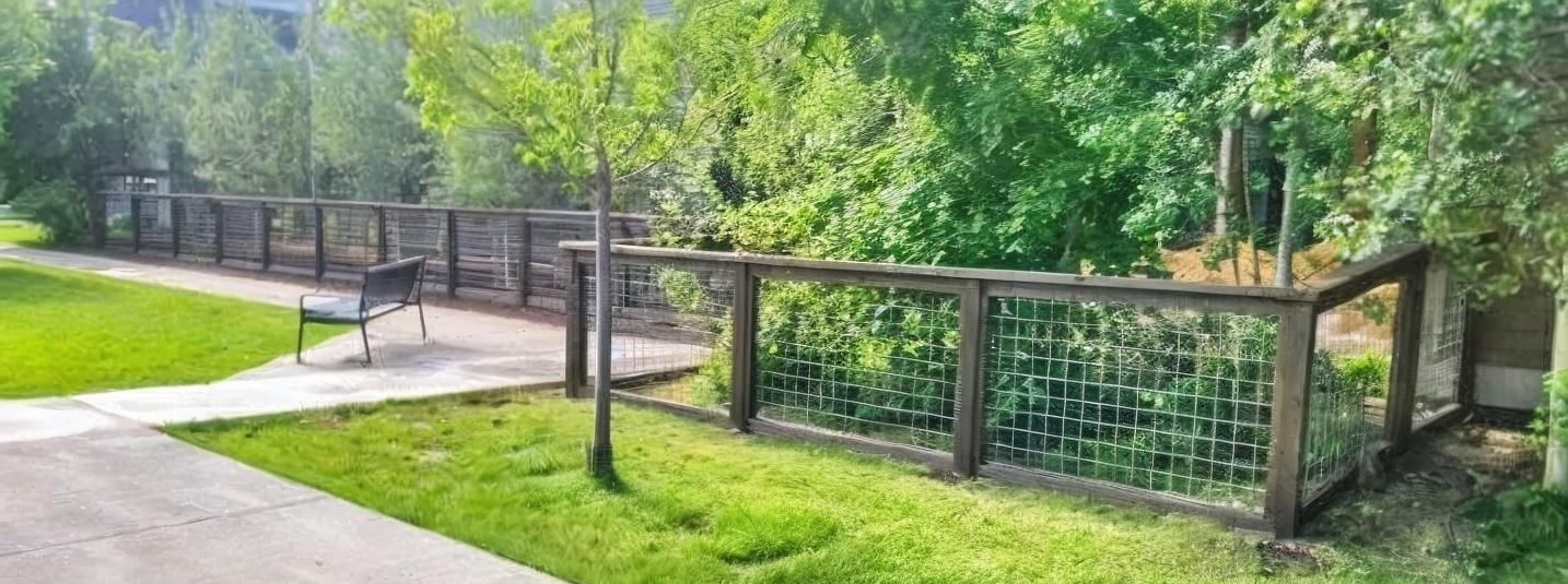 Park walkway with a wooden fence and gate beside a grassy, tree-lined path