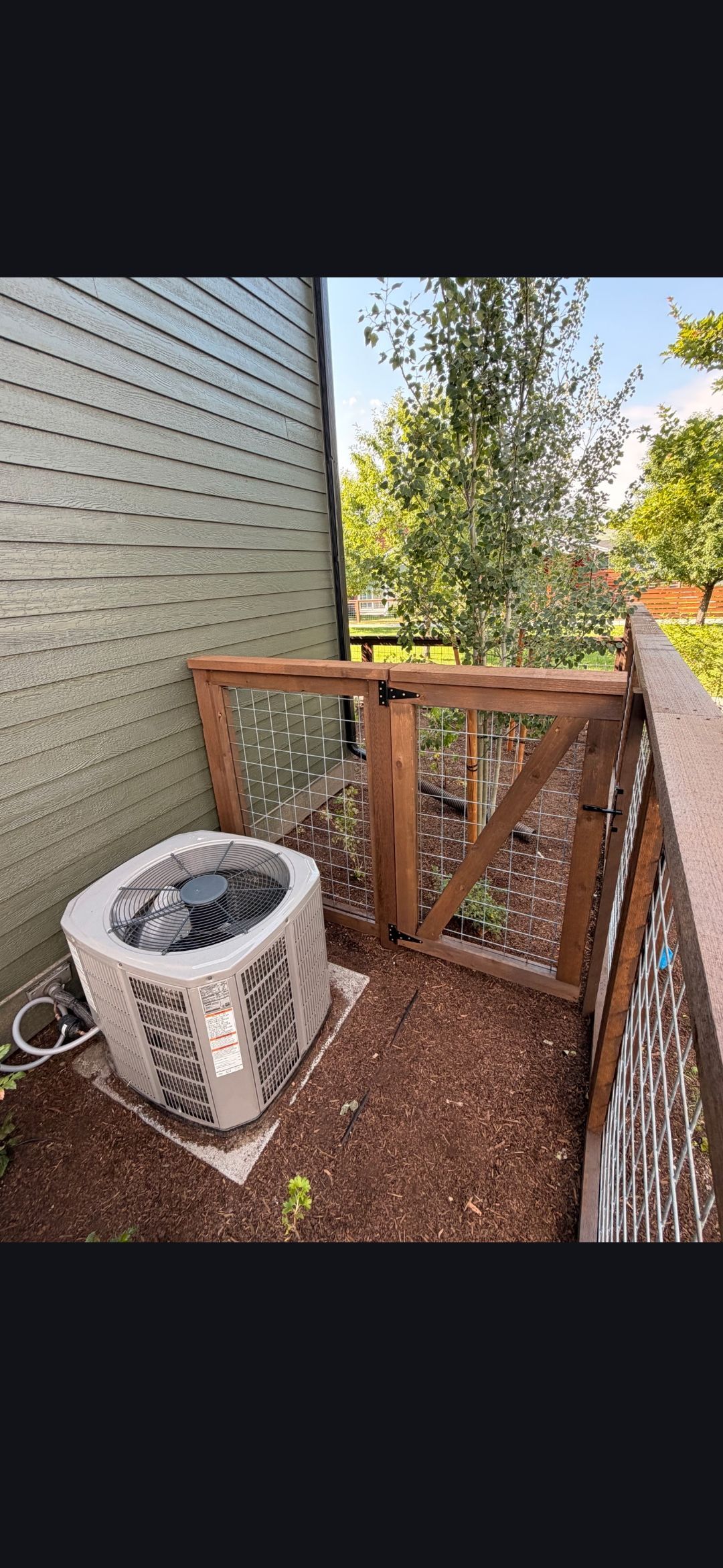 Small fenced patio with a square planter and gravel beside a house wall and wooden gate.