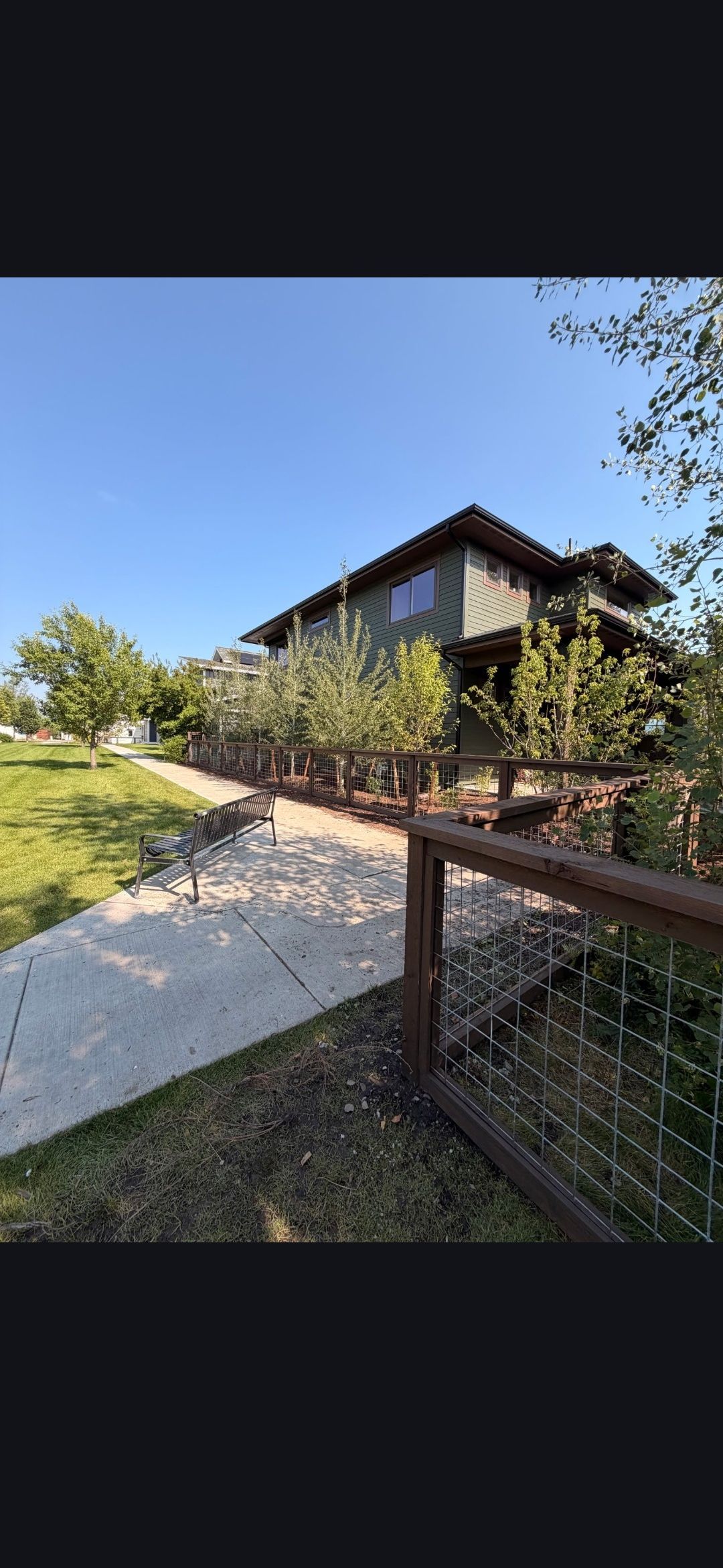 Modern house with a sloped roof beside a path and wooden fence under a clear blue sky