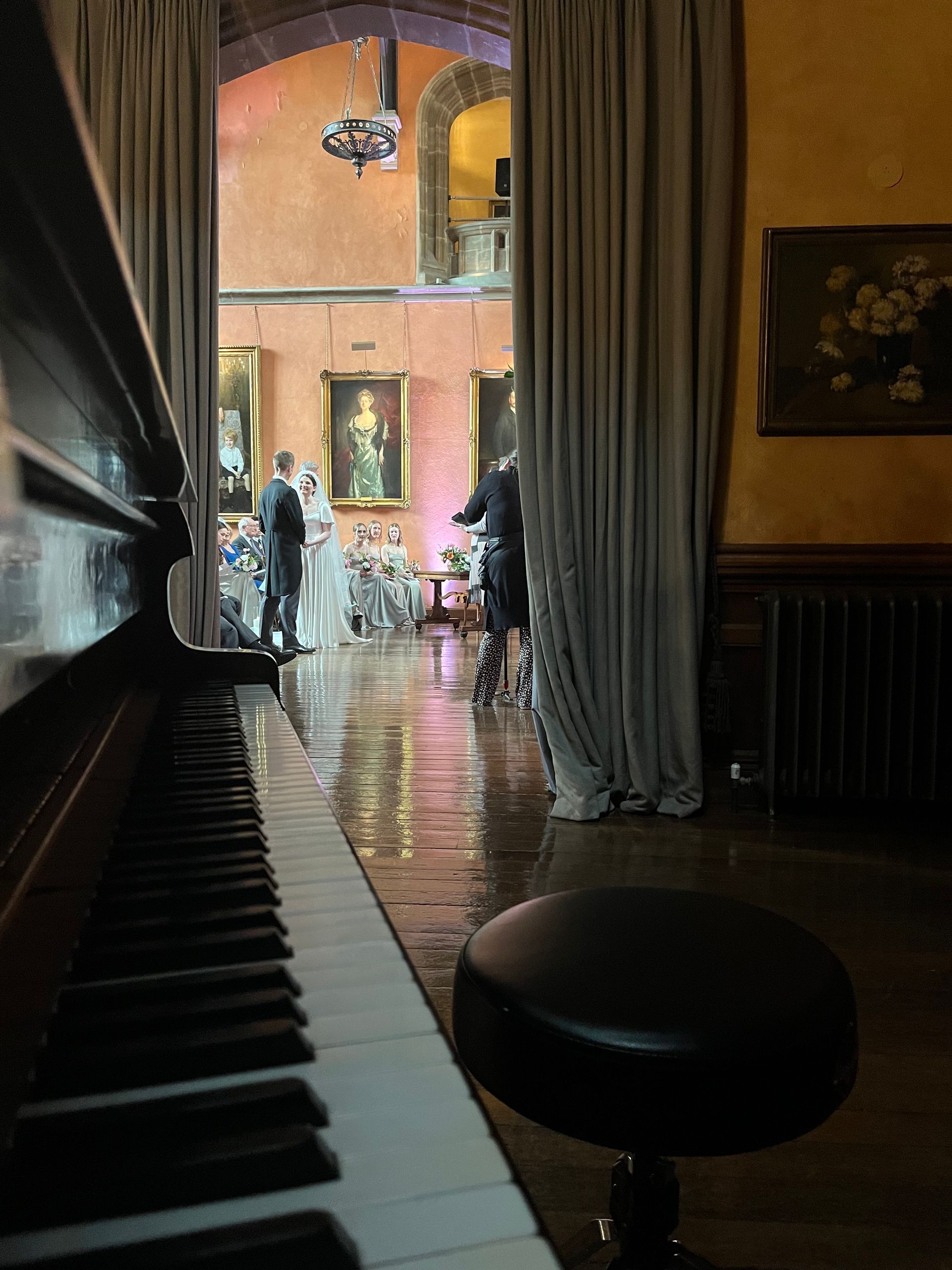 A piano in the foreground overlooks a bride and groom in a grand hall