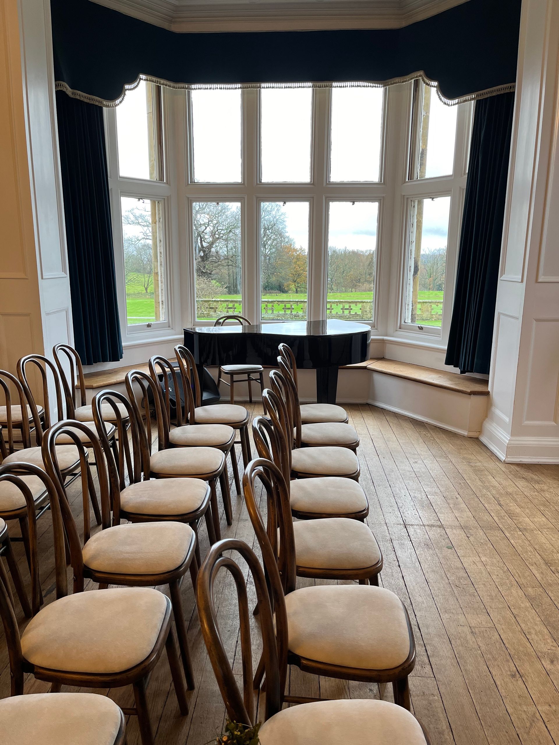 A grand piano in the bay window of a room set up for a wedding ceremony
