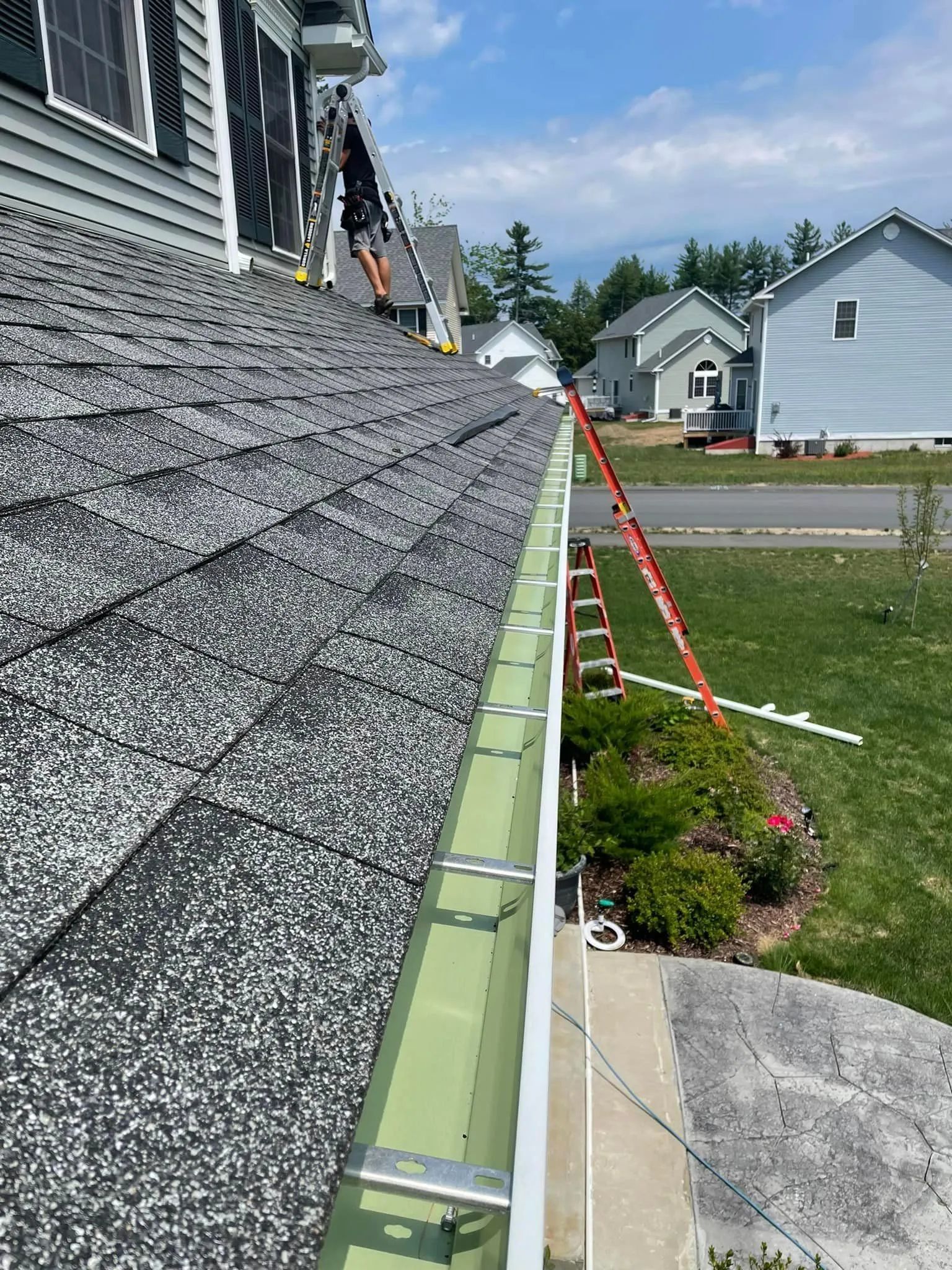 Roofing work on a house with green gutters, a ladder, and shingles along the roof edge