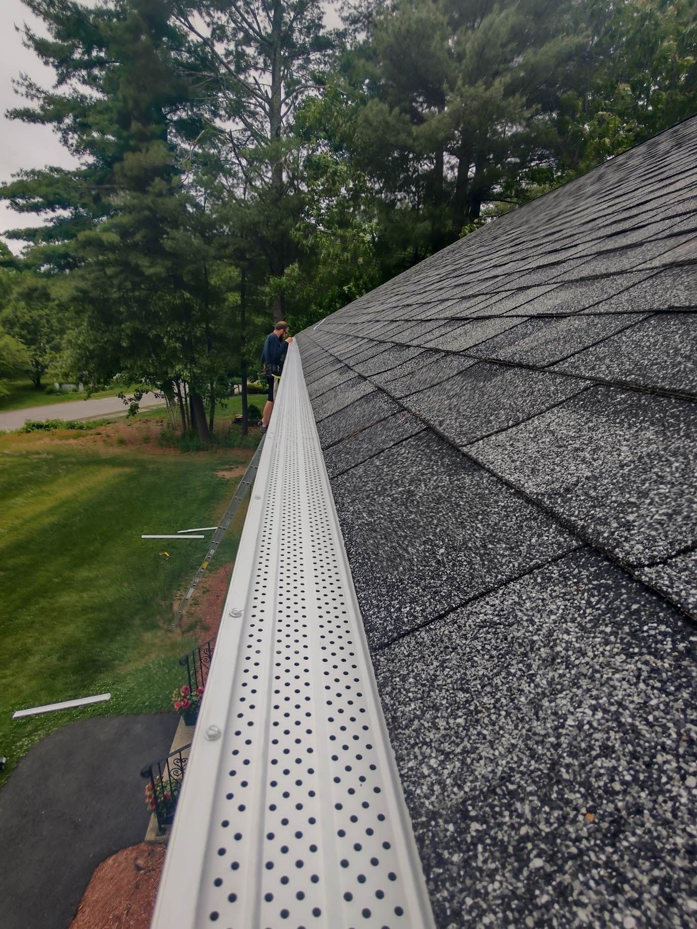 A man is standing on the roof of a house with a gutter.