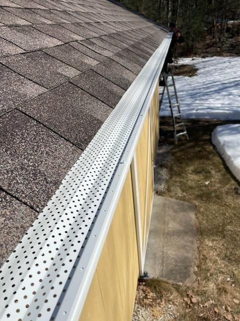 A gutter on the side of a building with a ladder in the background.