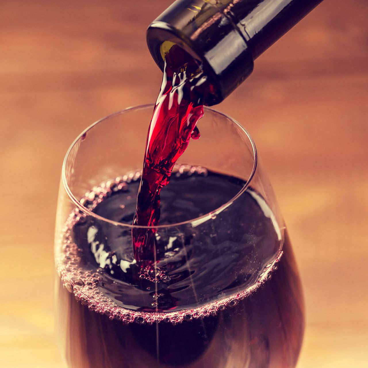 Primo piano di vino rosso versato da una bottiglia in un bicchiere trasparente.
