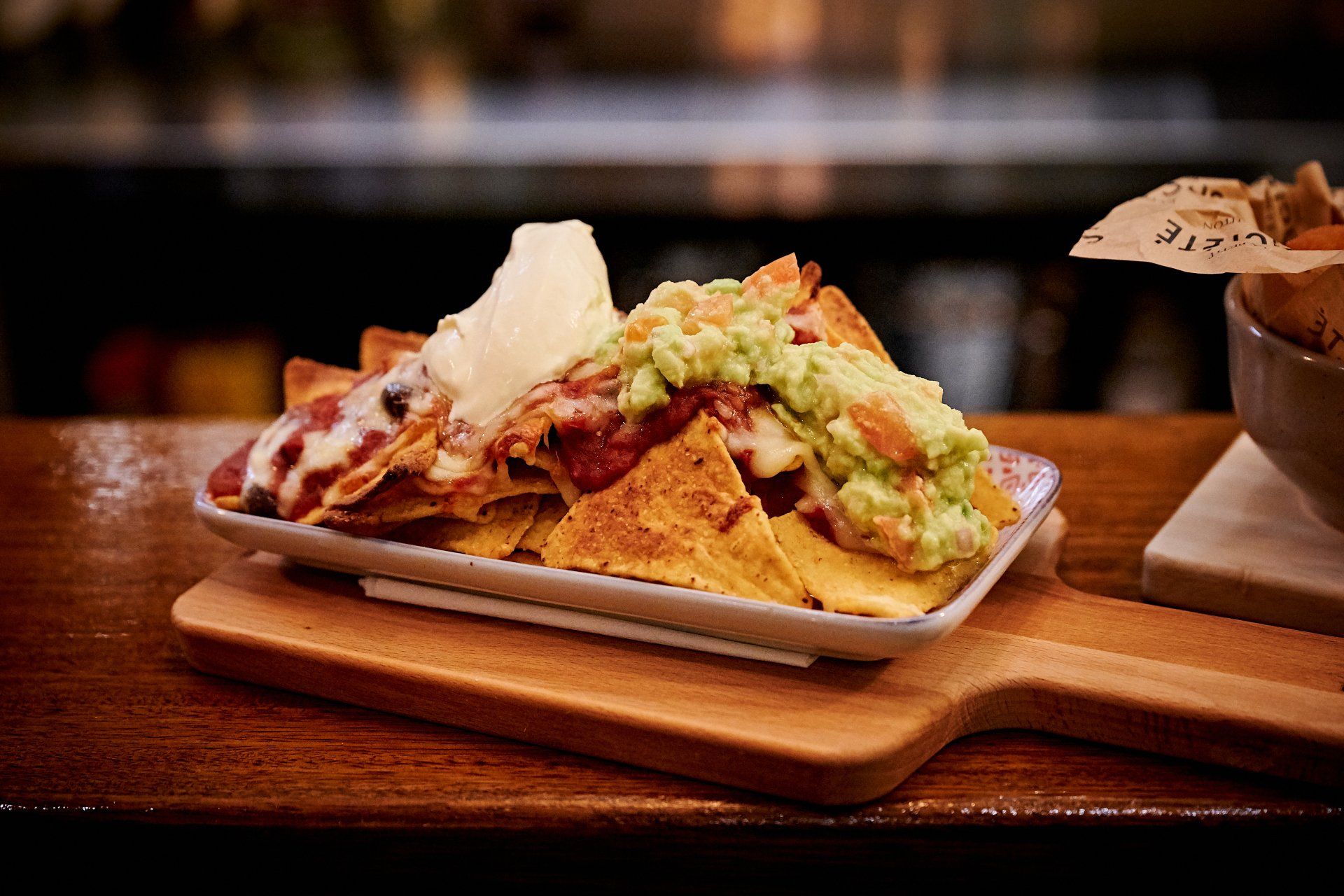 Nachos with guacamole, cheese, and sauce on a wooden serving board.