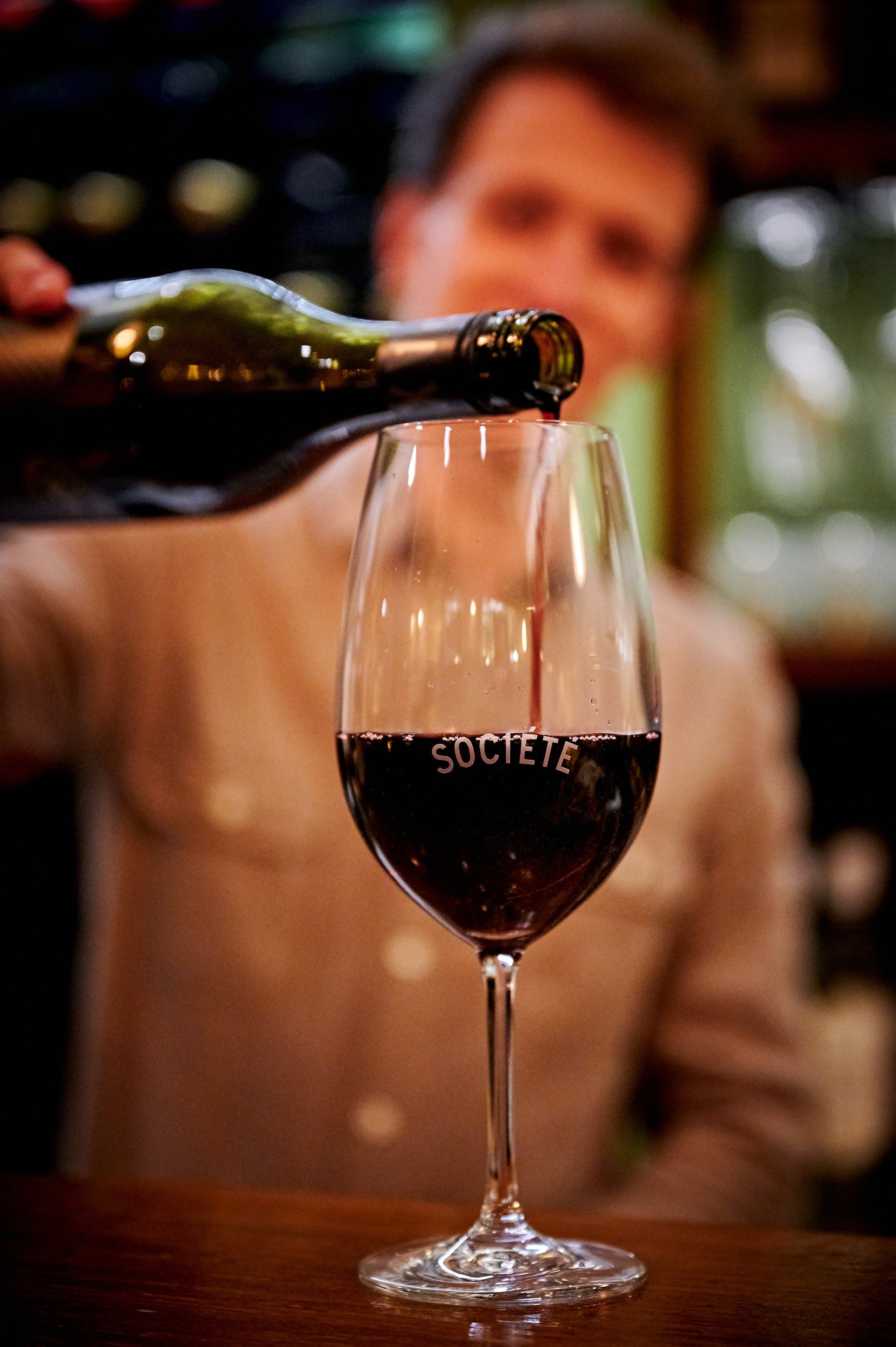 Man pouring red wine into a glass labeled 