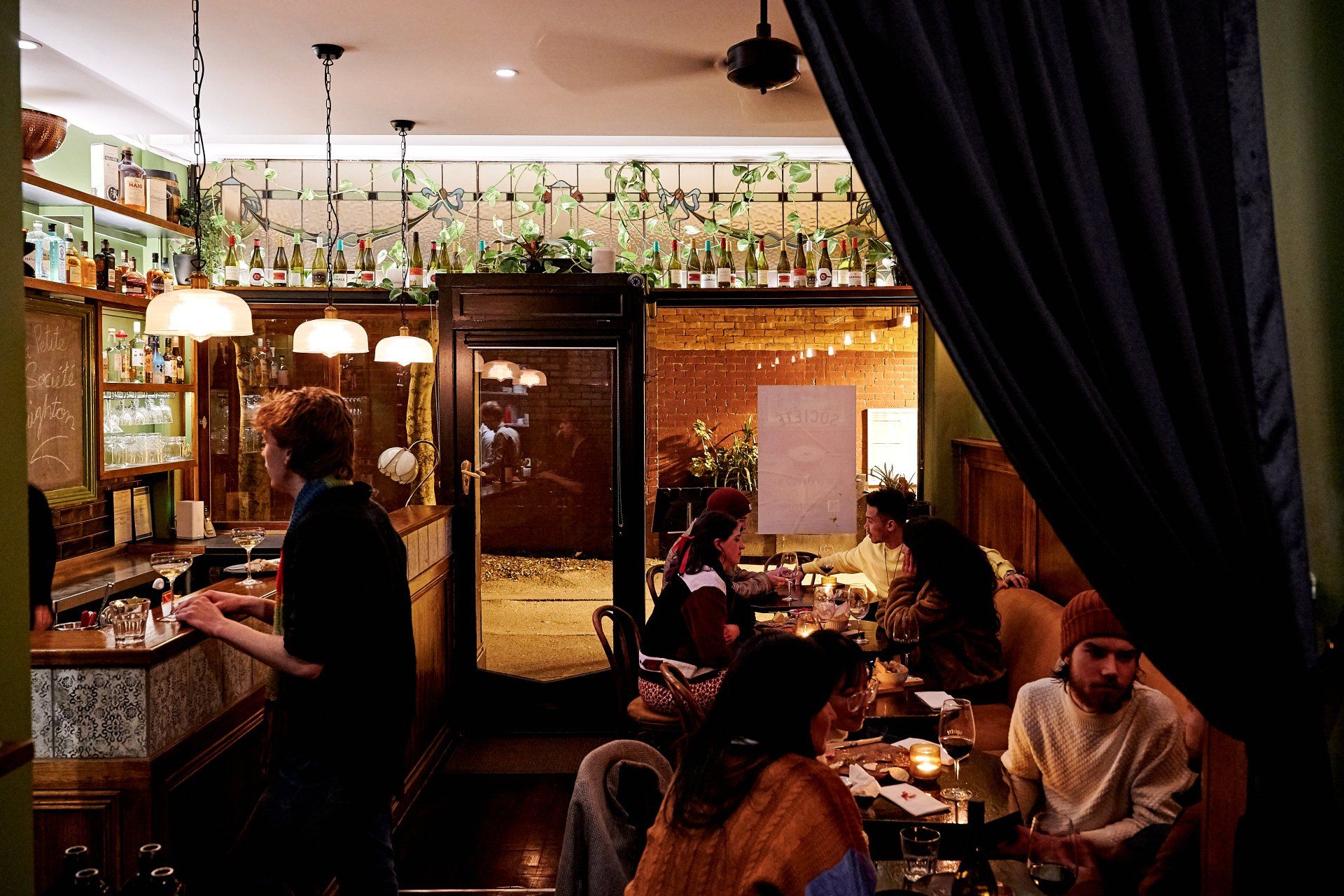 Interior of a dimly lit wine bar with patrons. A bartender works, while others sit and converse.