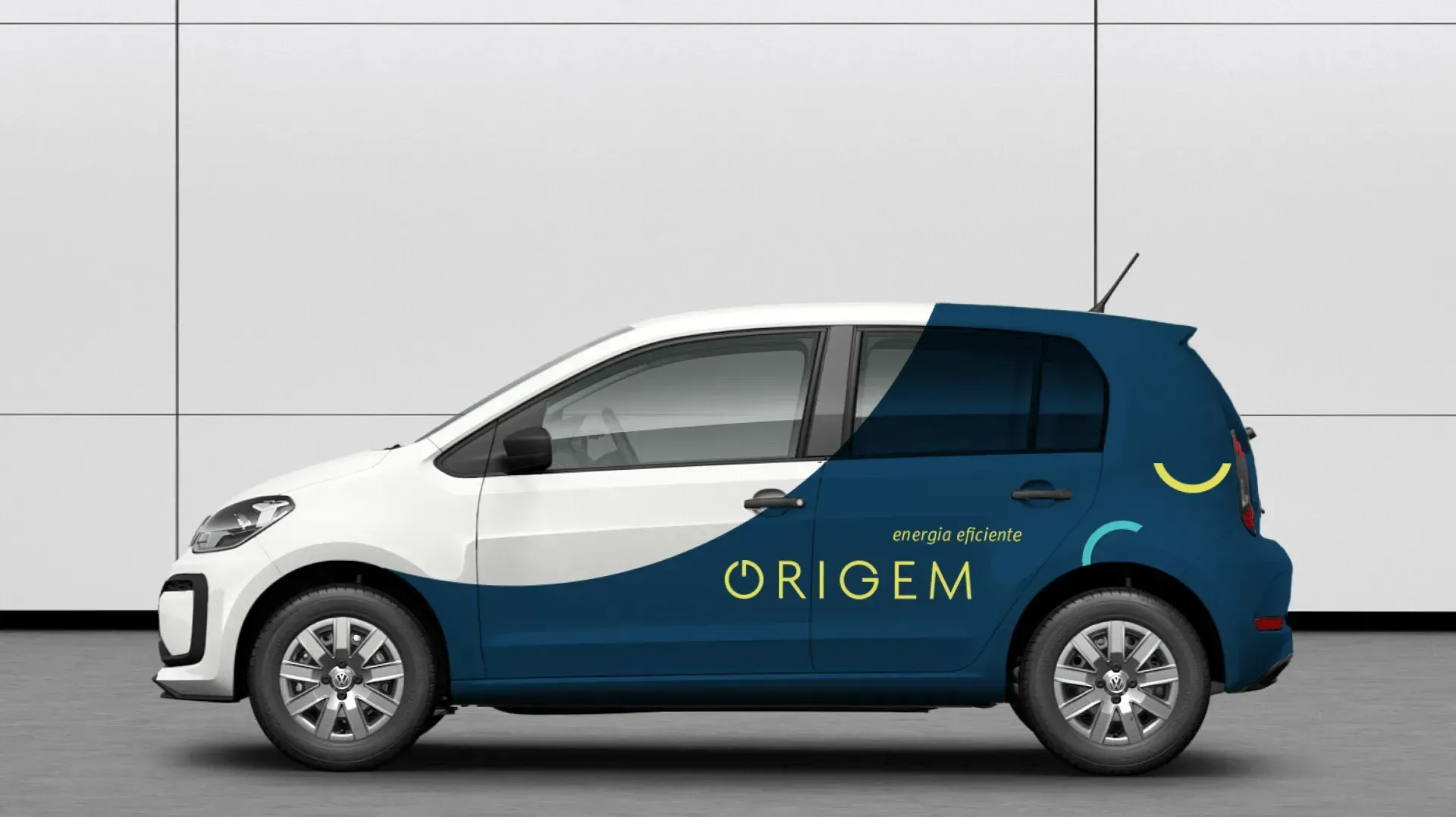 Um carro azul e branco com a palavra origem na lateral está estacionado em frente a um muro branco.