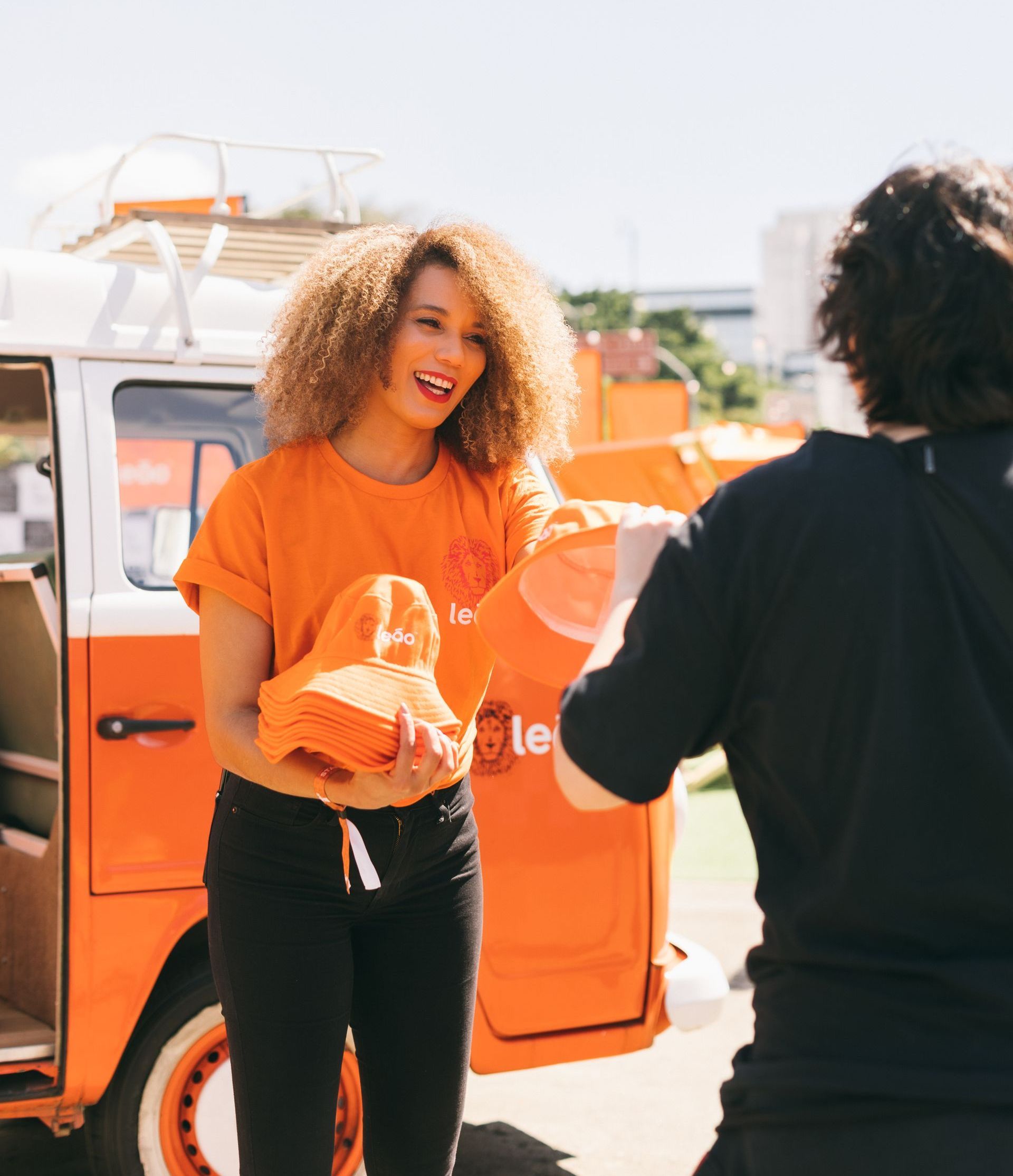 Uma mulher com uma camisa laranja está parada na frente de uma van laranja
