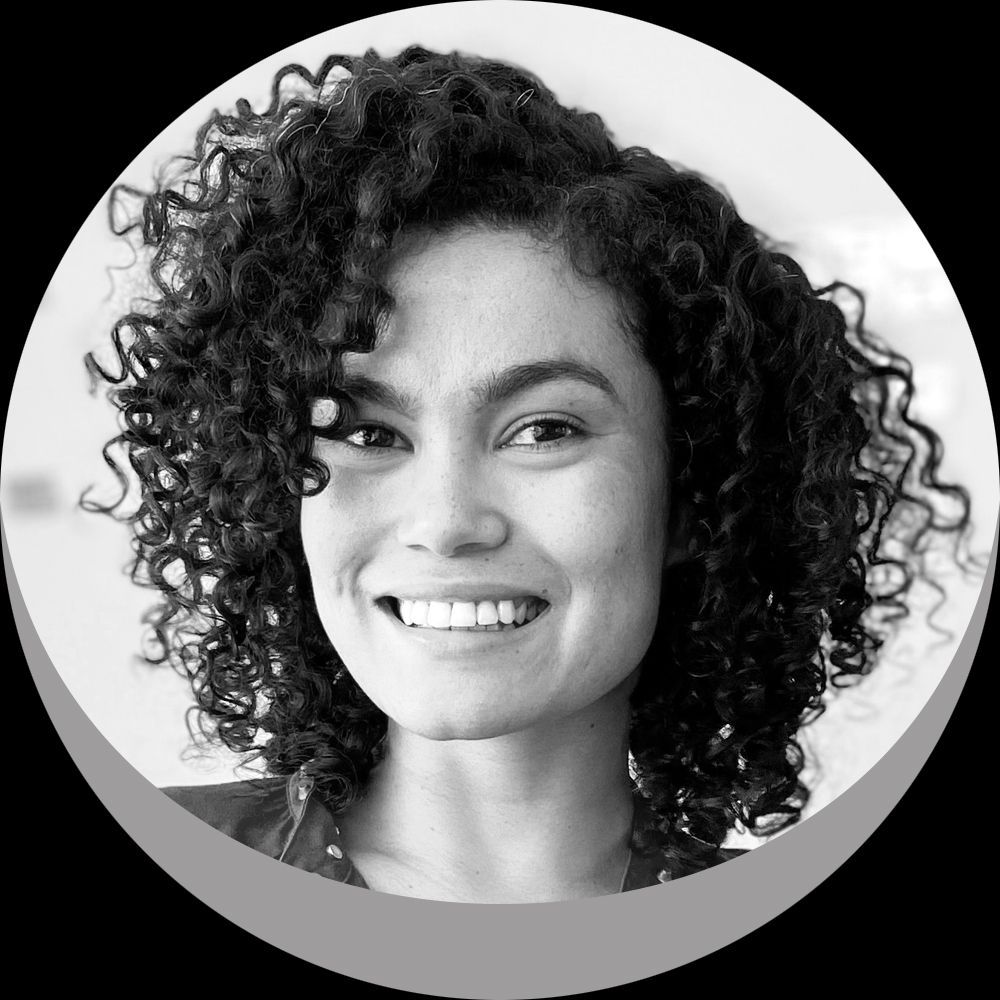 Uma mulher com cabelos cacheados está sorrindo em uma foto em preto e branco.