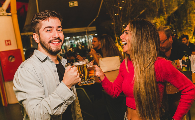 Um homem e uma mulher estão brindando com cerveja em um bar.