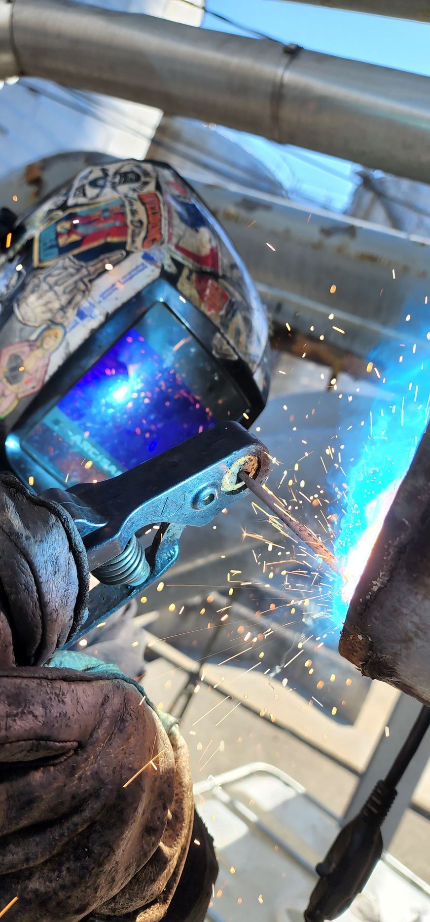 A man wearing a welding helmet is welding a piece of metal.