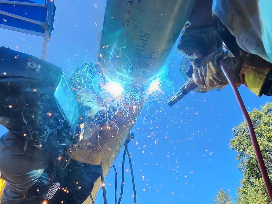 A man is welding a pipe with a welding mask on.
