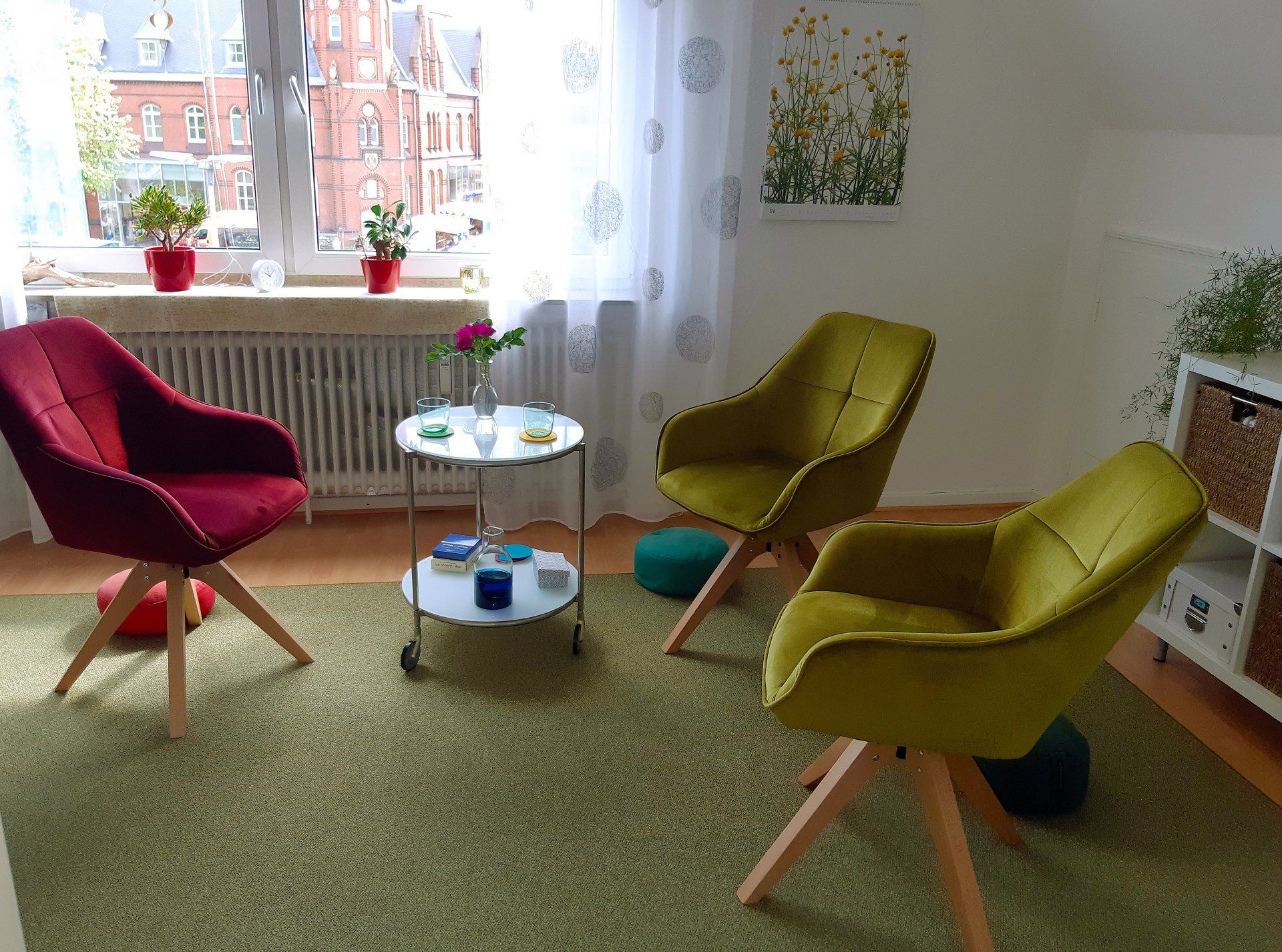 Gemütliches Zimmer mit drei farbenfrohen Sesseln um einen kleinen runden Tisch am Fenster