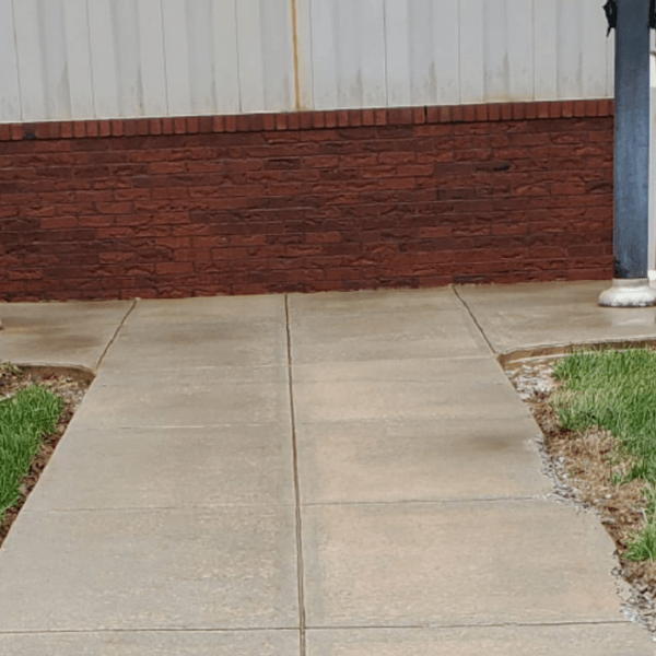 a brick wall is behind a clean concrete walkway .