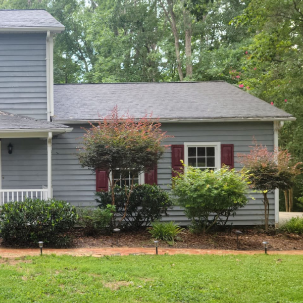 a gray house with red shutters and a large lawn in front of it .