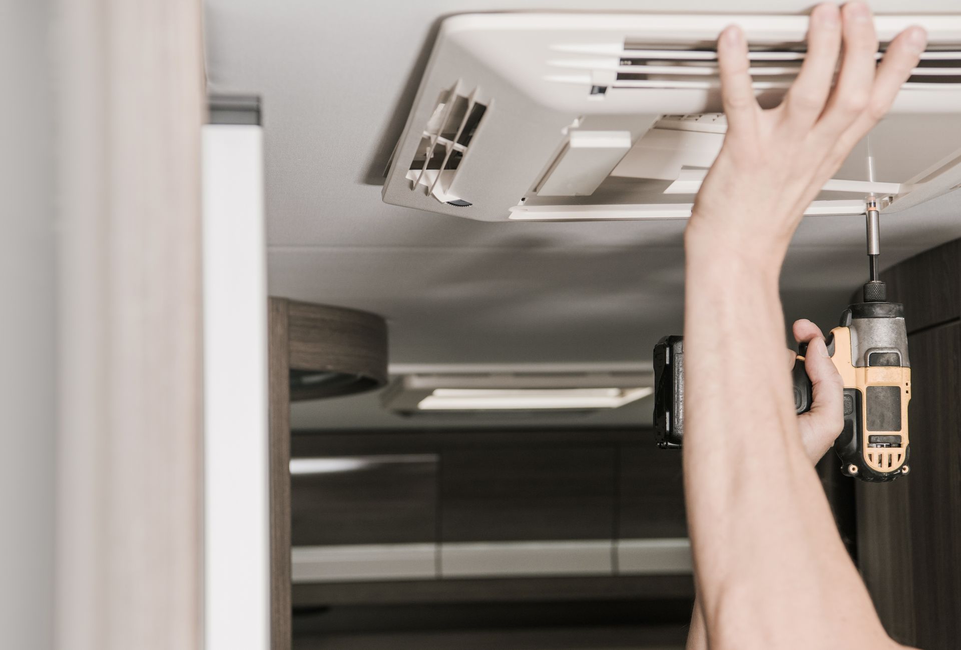 A person is fixing a ceiling fan with a drill.