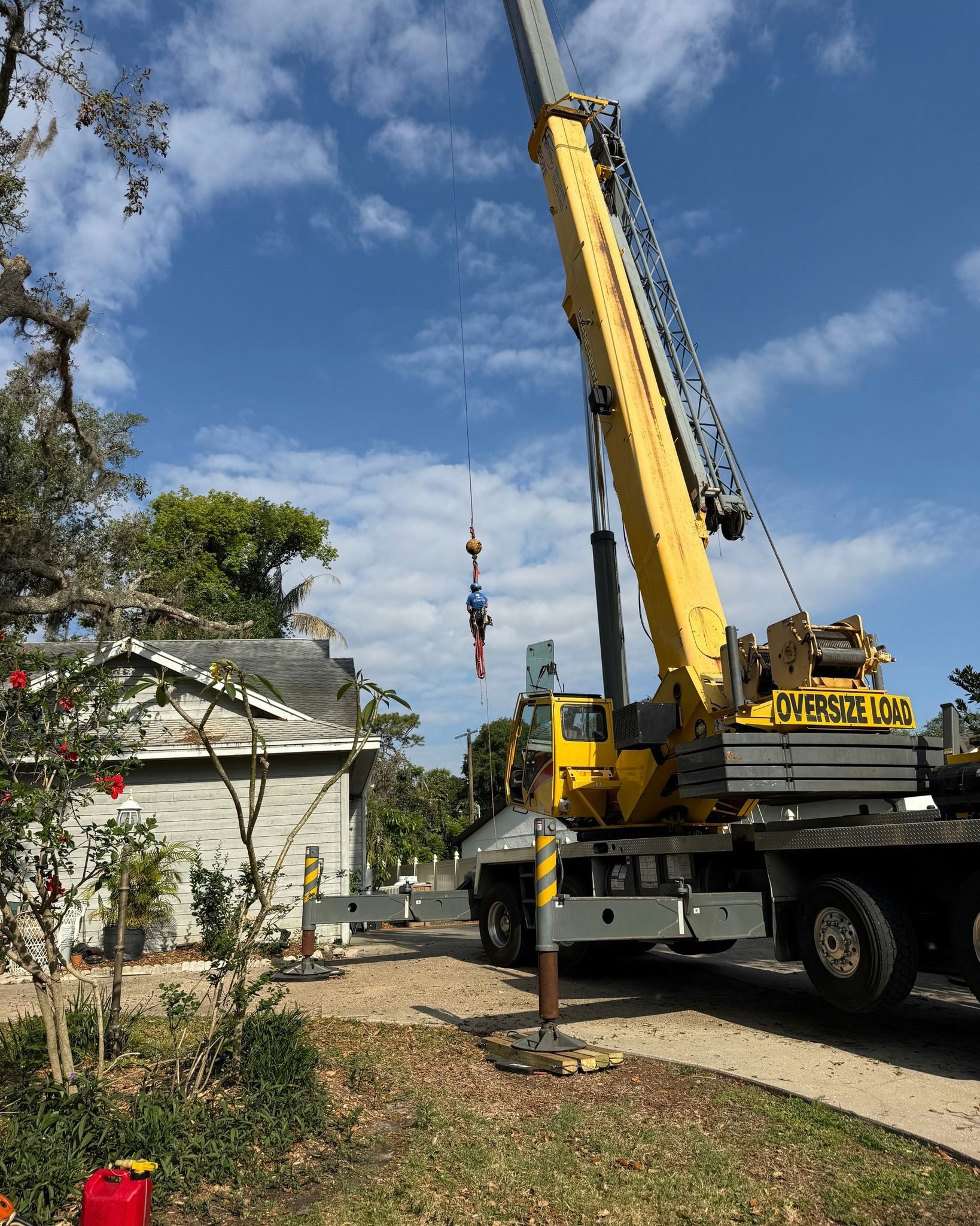 Yellow crane truck lifting a load beside a house on a sunny residential street