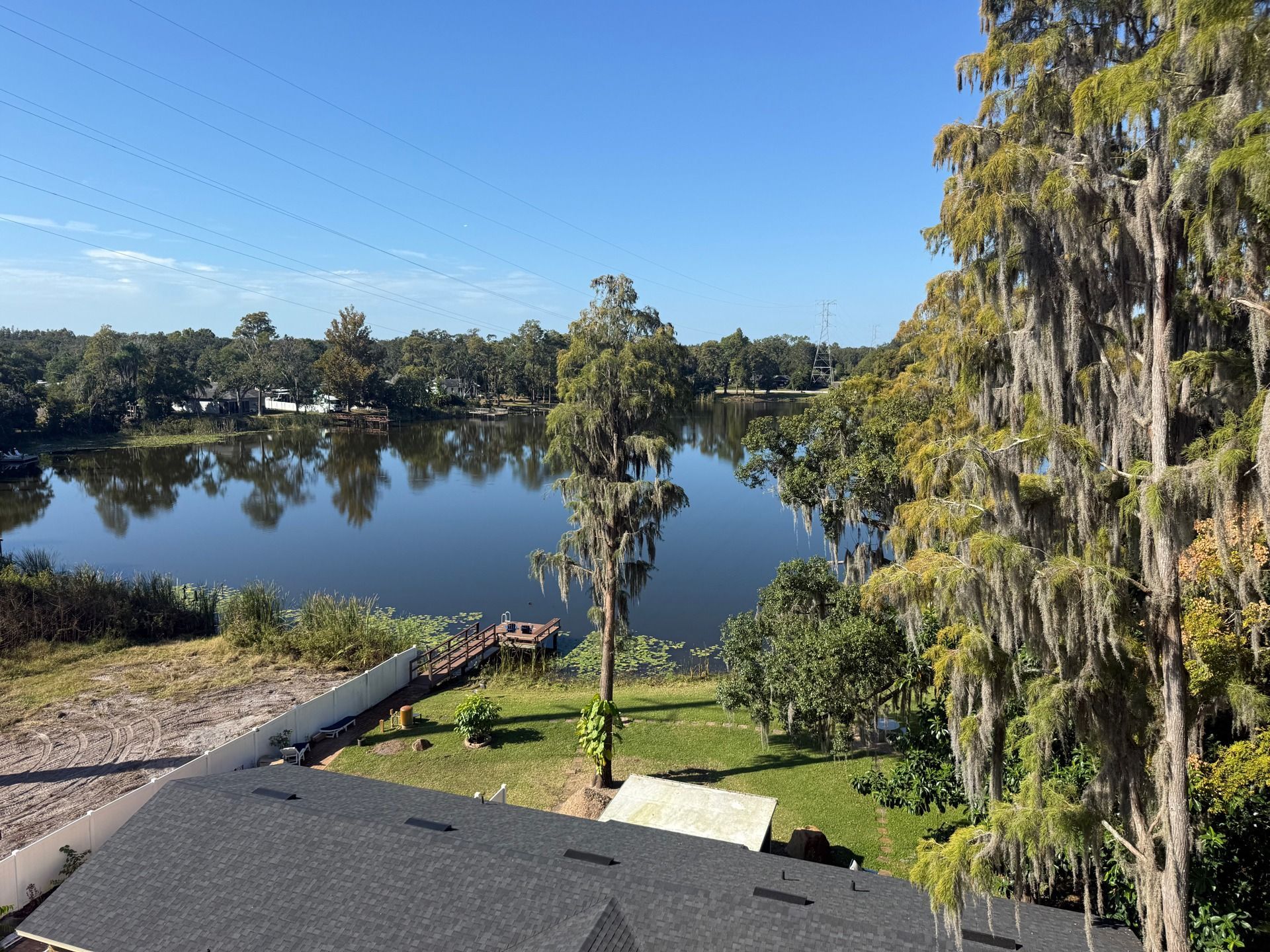 Lake view from a rooftop with trees, blue sky, and a grassy shoreline reflected in calm water