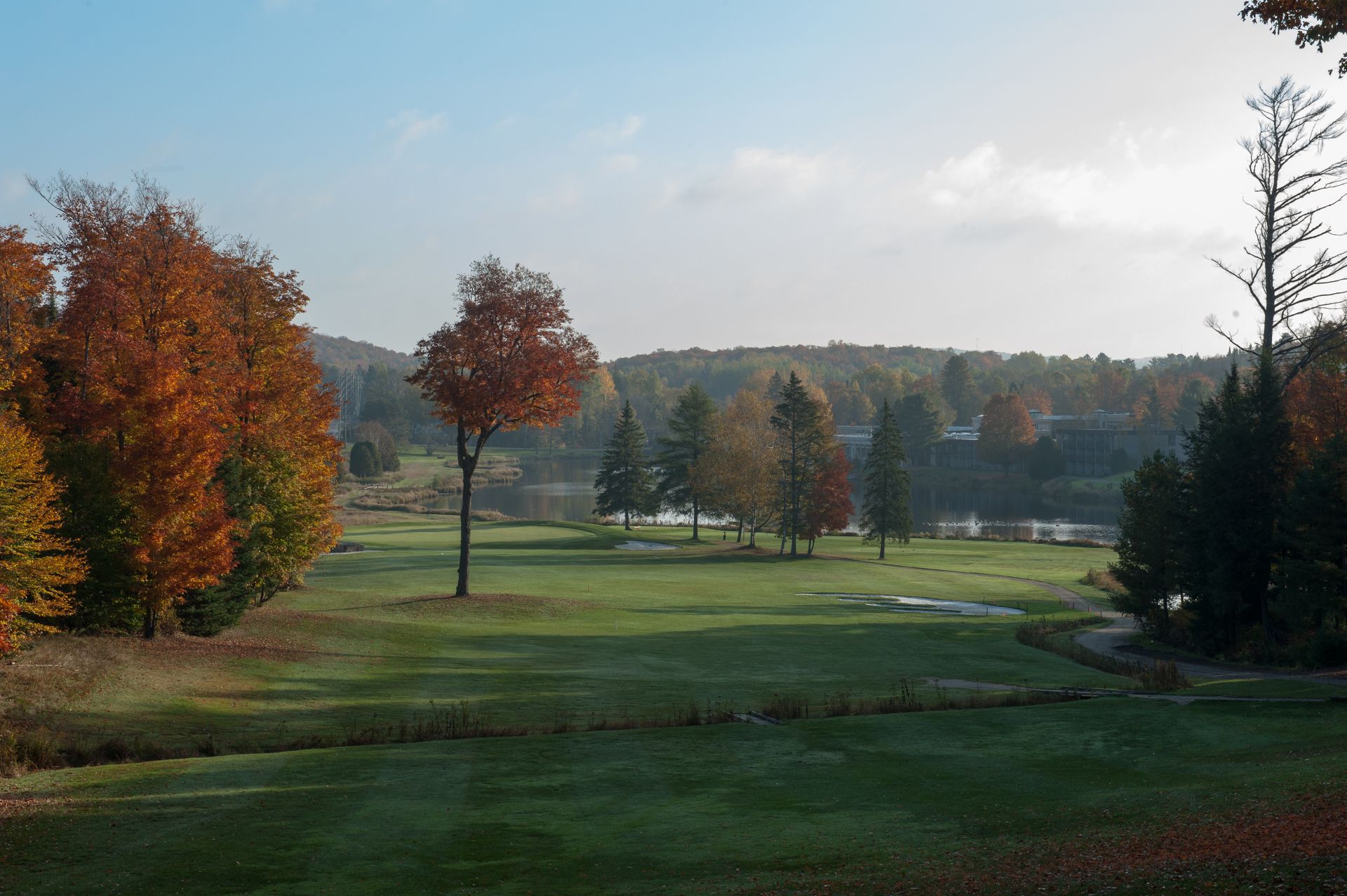A golf course with trees and a lake in the background on a sunny day.