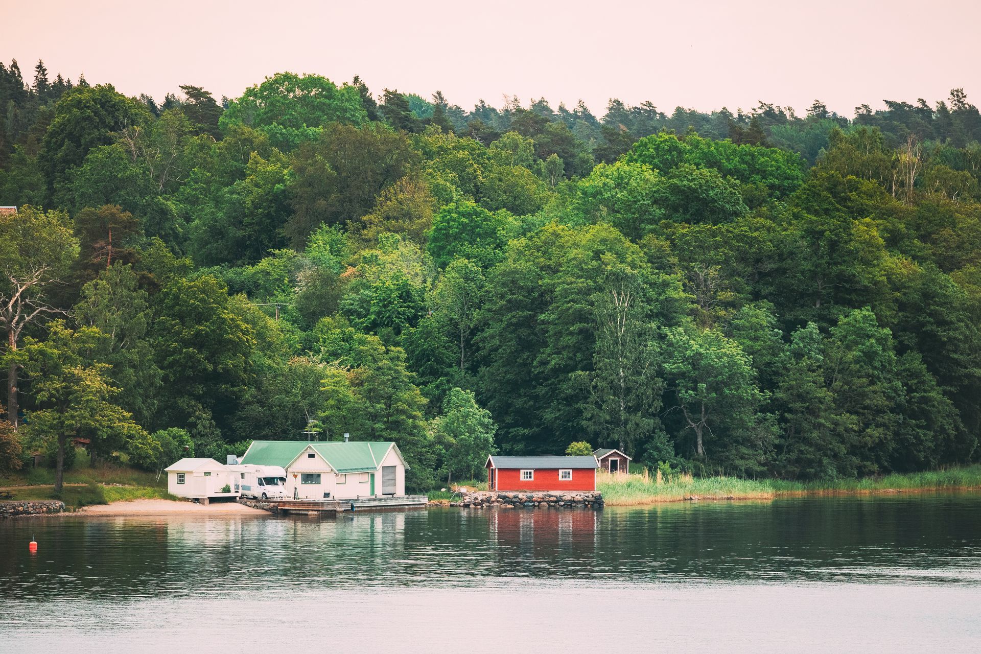 A red and white house sits on a small island in the middle of a lake surrounded by trees.