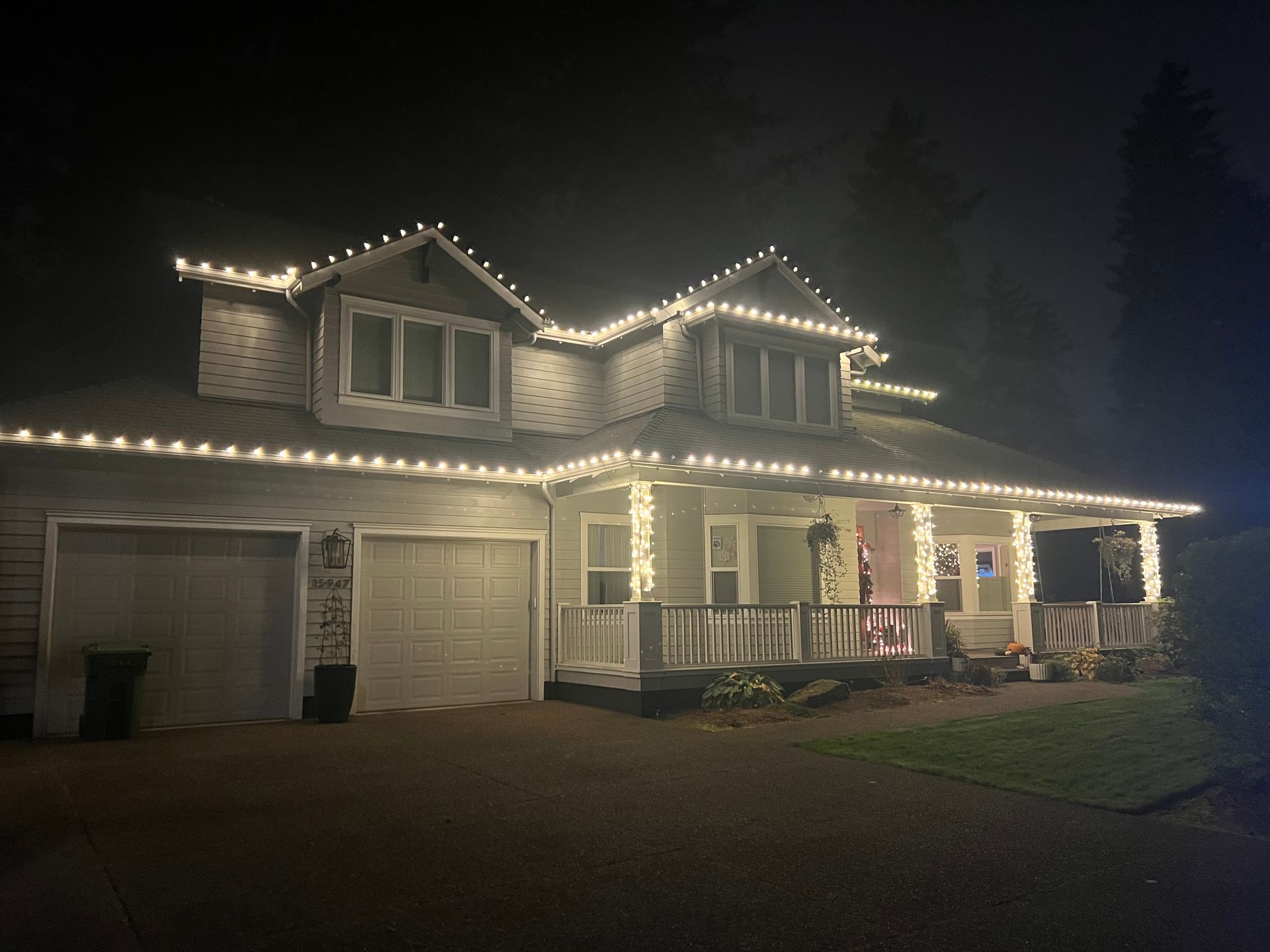 Two-story house at night outlined with white Christmas lights, with garage and front porch visible