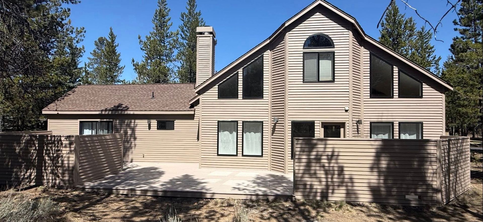 Two-story beige house with a stone porch and tall evergreen trees in front