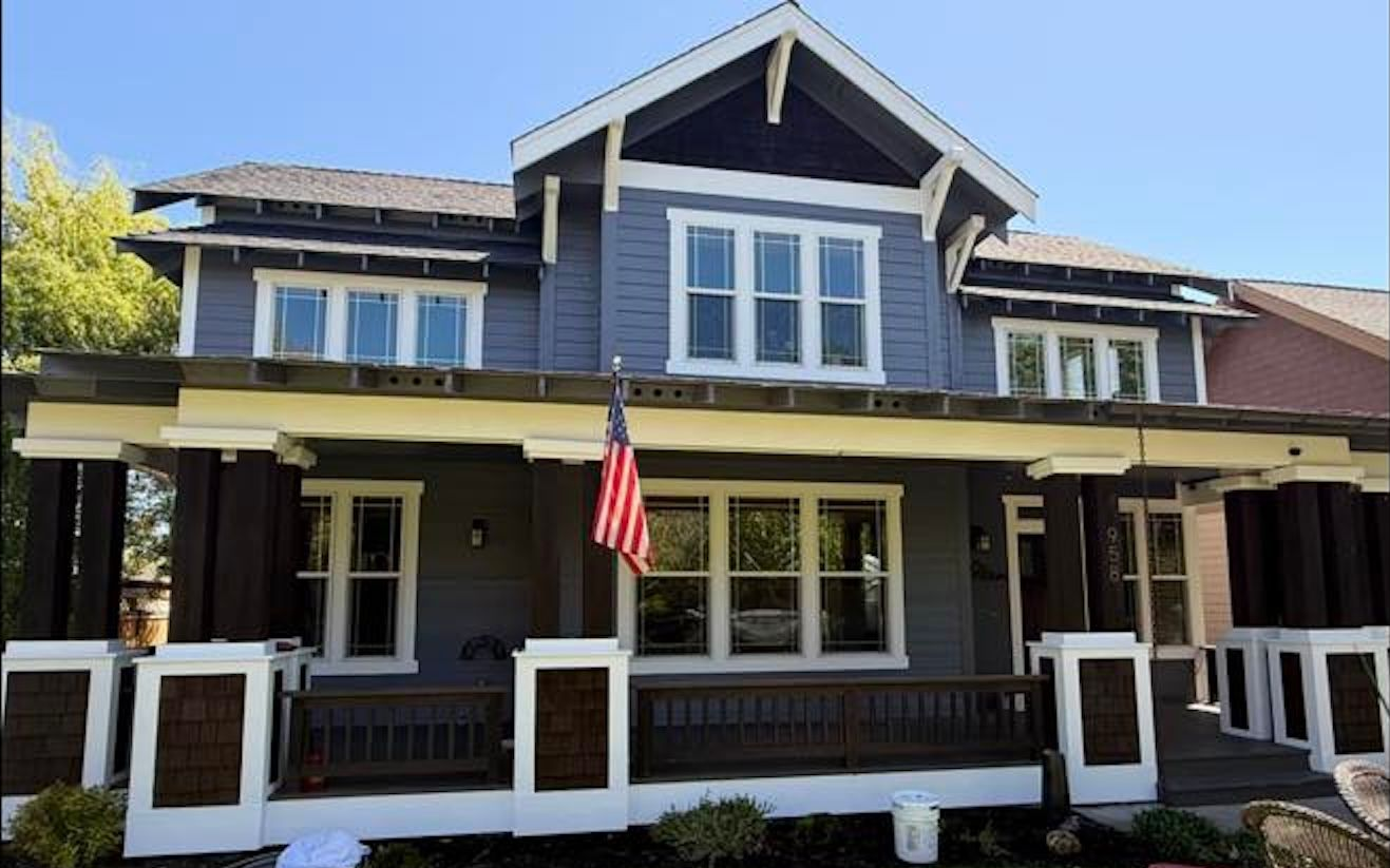 Blue-gray house with white trim, covered porch, and an American flag hanging by the front door.