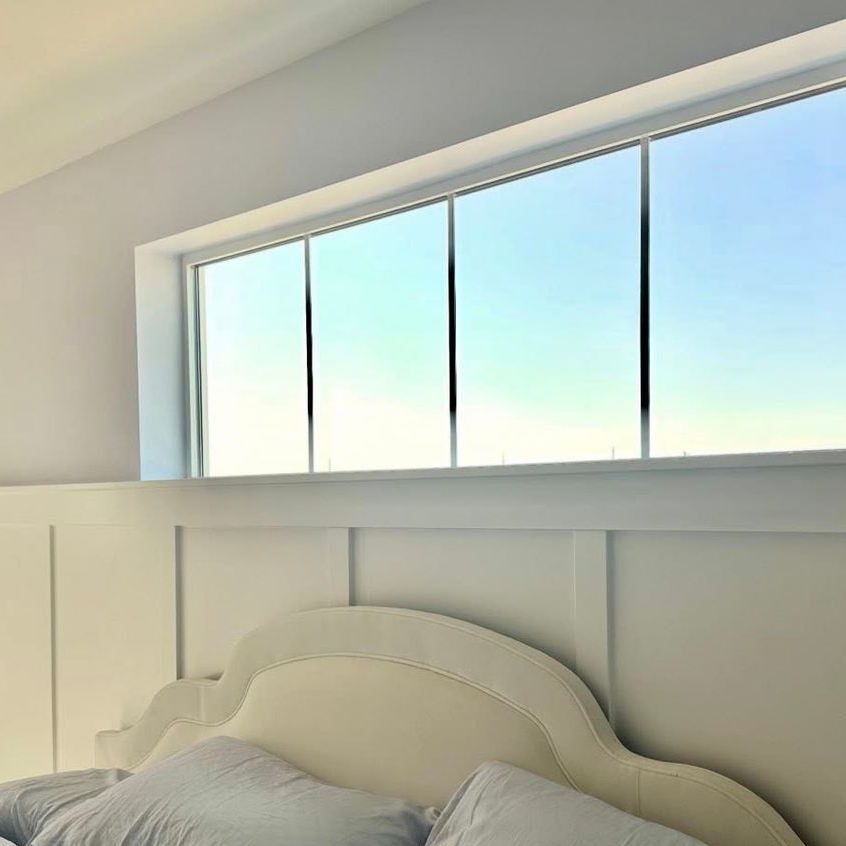 Bright bedroom with a bed under a large window and white paneled wall