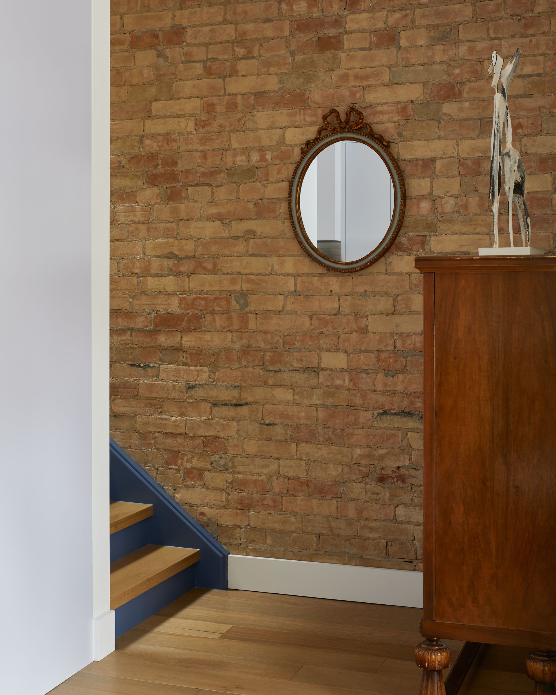 A brick wall with a mirror and a wooden dresser