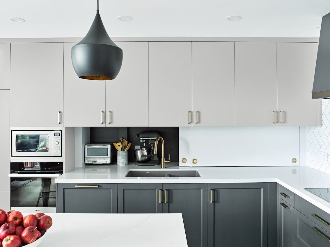 A kitchen with gray cabinets and white counter tops and a bowl of apples on the counter.