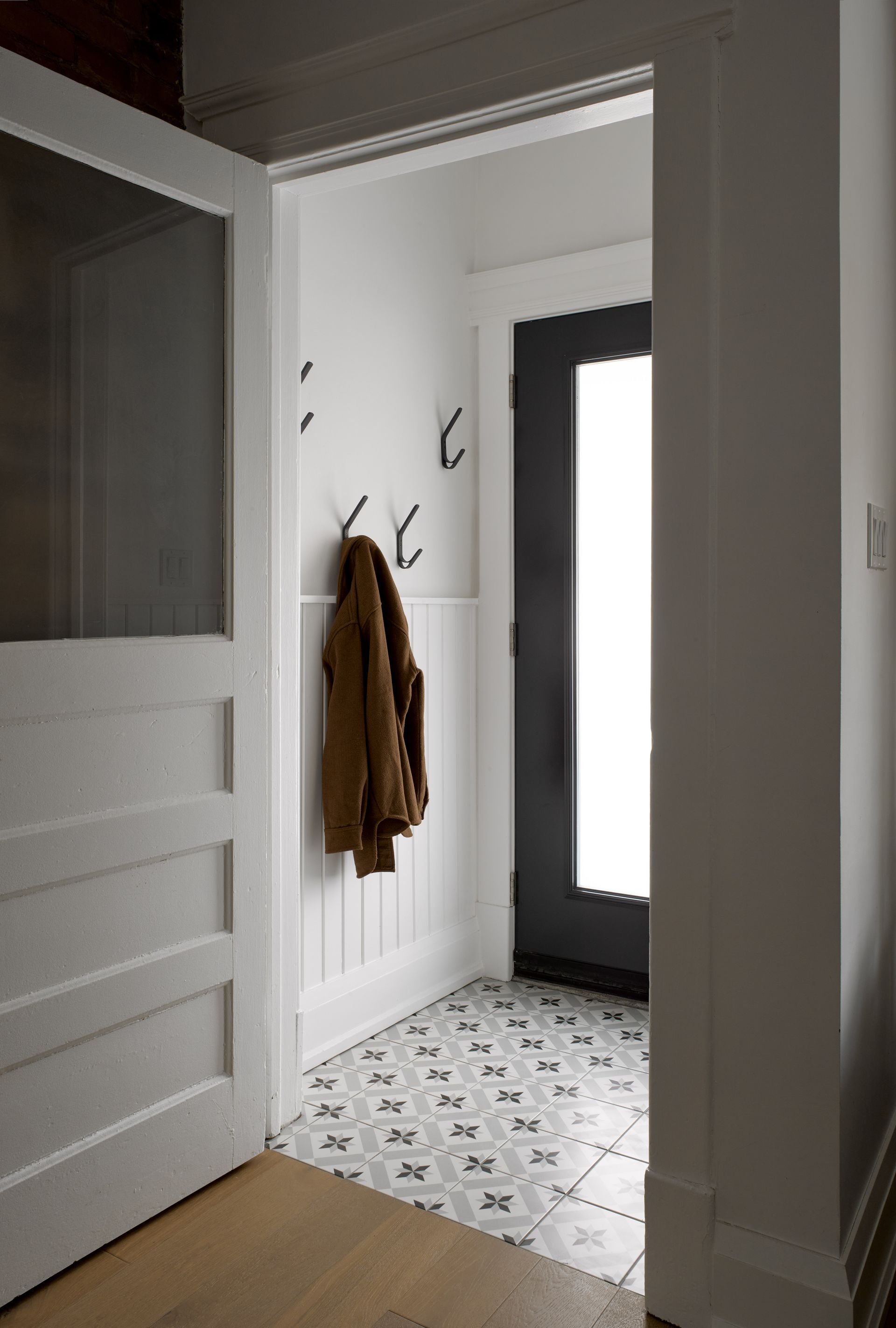A coat is hanging on a hook in a hallway next to a door.