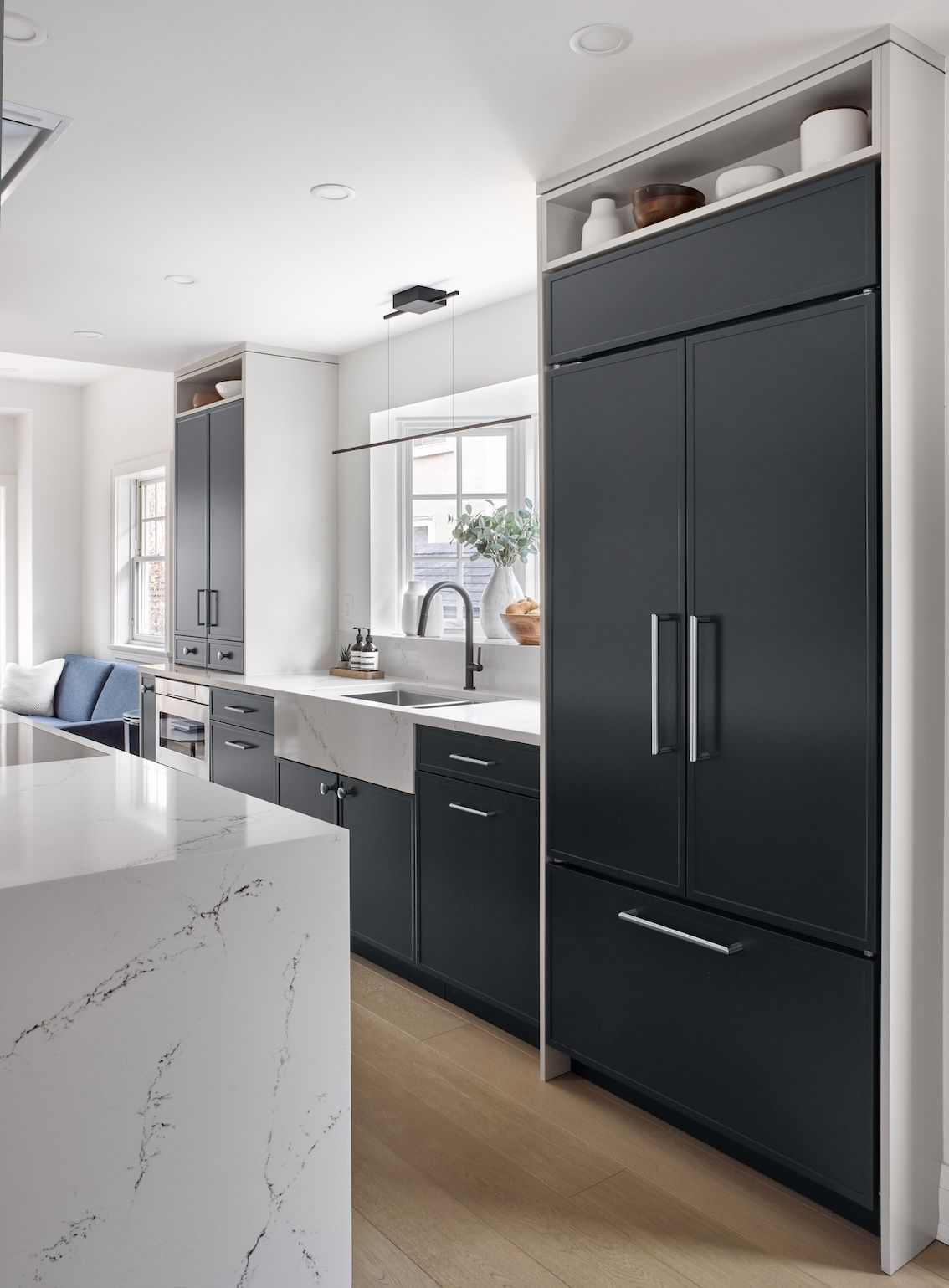 A kitchen with black cabinets , white counter tops , a sink and a refrigerator.
