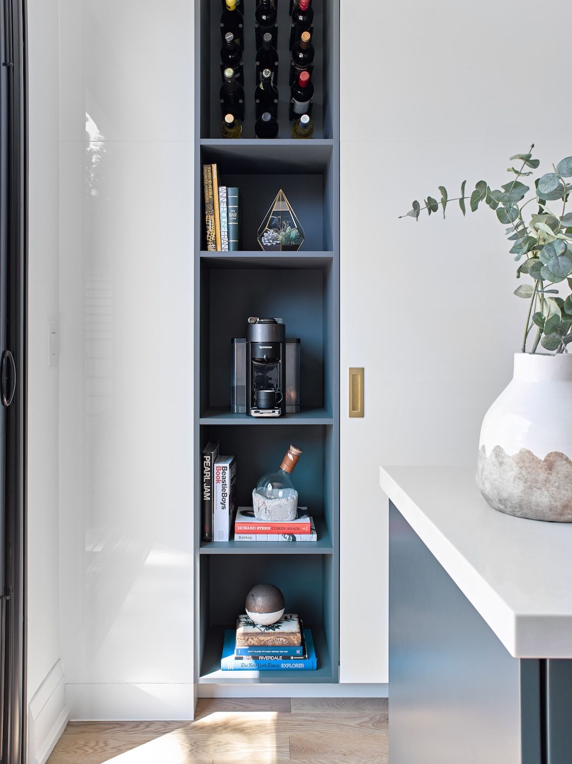 A kitchen with a shelf filled with books and wine bottles.